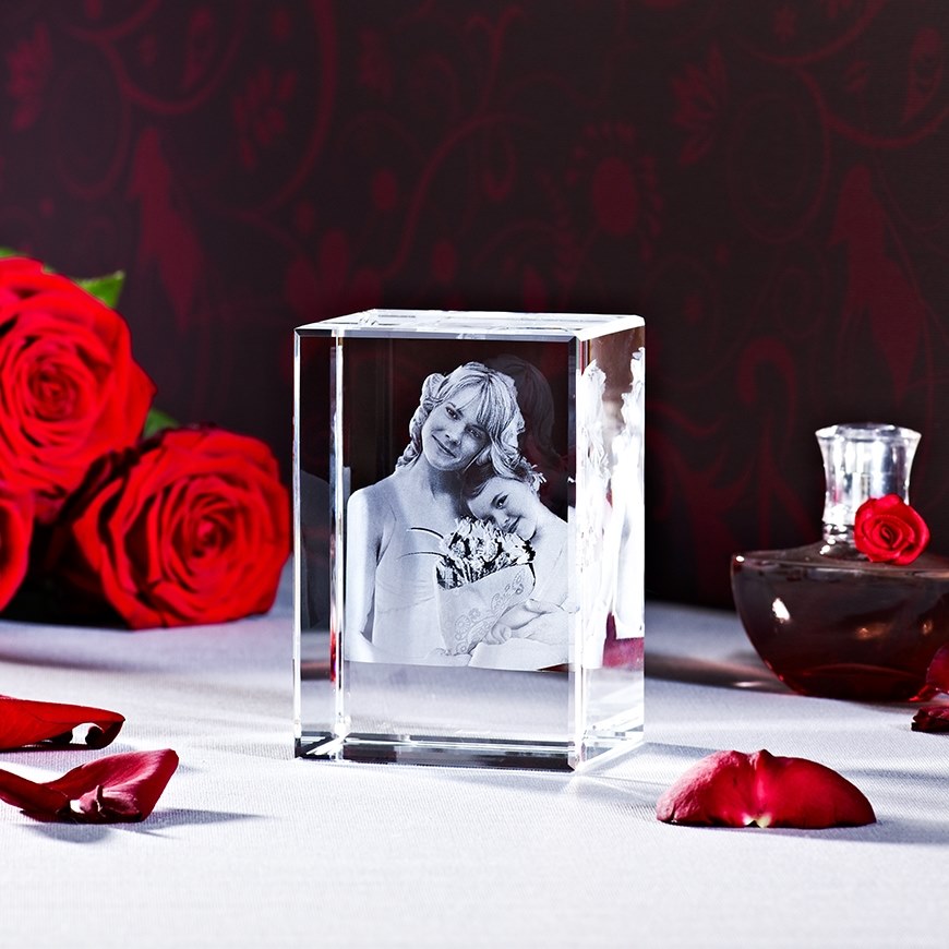 Kristallwürfel mit 3D-Gravur eines Mutter-Kind-Porträts, umgeben von roten Rosen und Rosenblättern auf weißem Untergrund